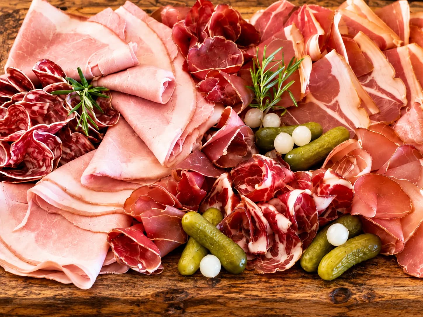 Saucissons secs suspendus à une poutre, jambon à l’os sur son support et rosette tranchée sur une ardoise
